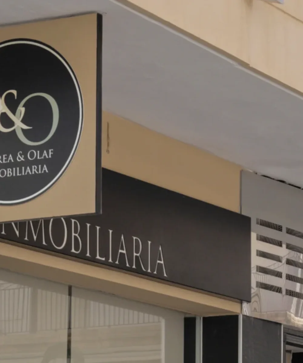 Enseigne extérieure de l'agence immobilière Andrea & Olaf, avec logo circulaire sur une façade en pierre noire et vitrine en verre.