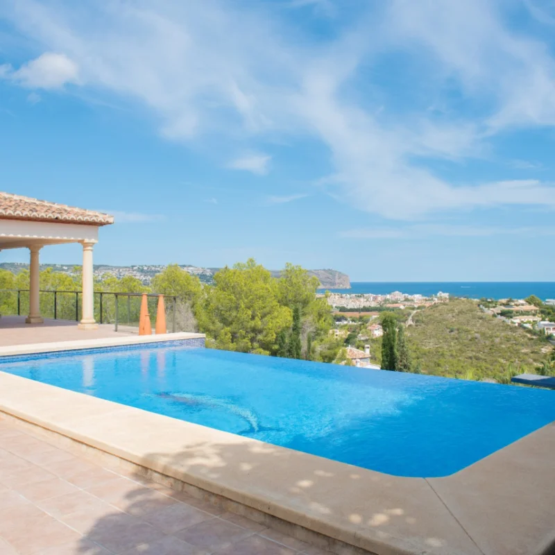 Piscina infinita con terraza de baldosas cerámicas y porche de columnas clásicas. Ofrece vistas panorámicas al mar Mediterráneo y la costa de Jávea.
