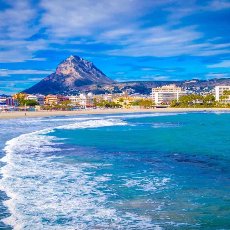 Vue panoramique de la plage de Jávea avec le Montgó en arrière-plan. Des immeubles résidentiels bordent la côte.