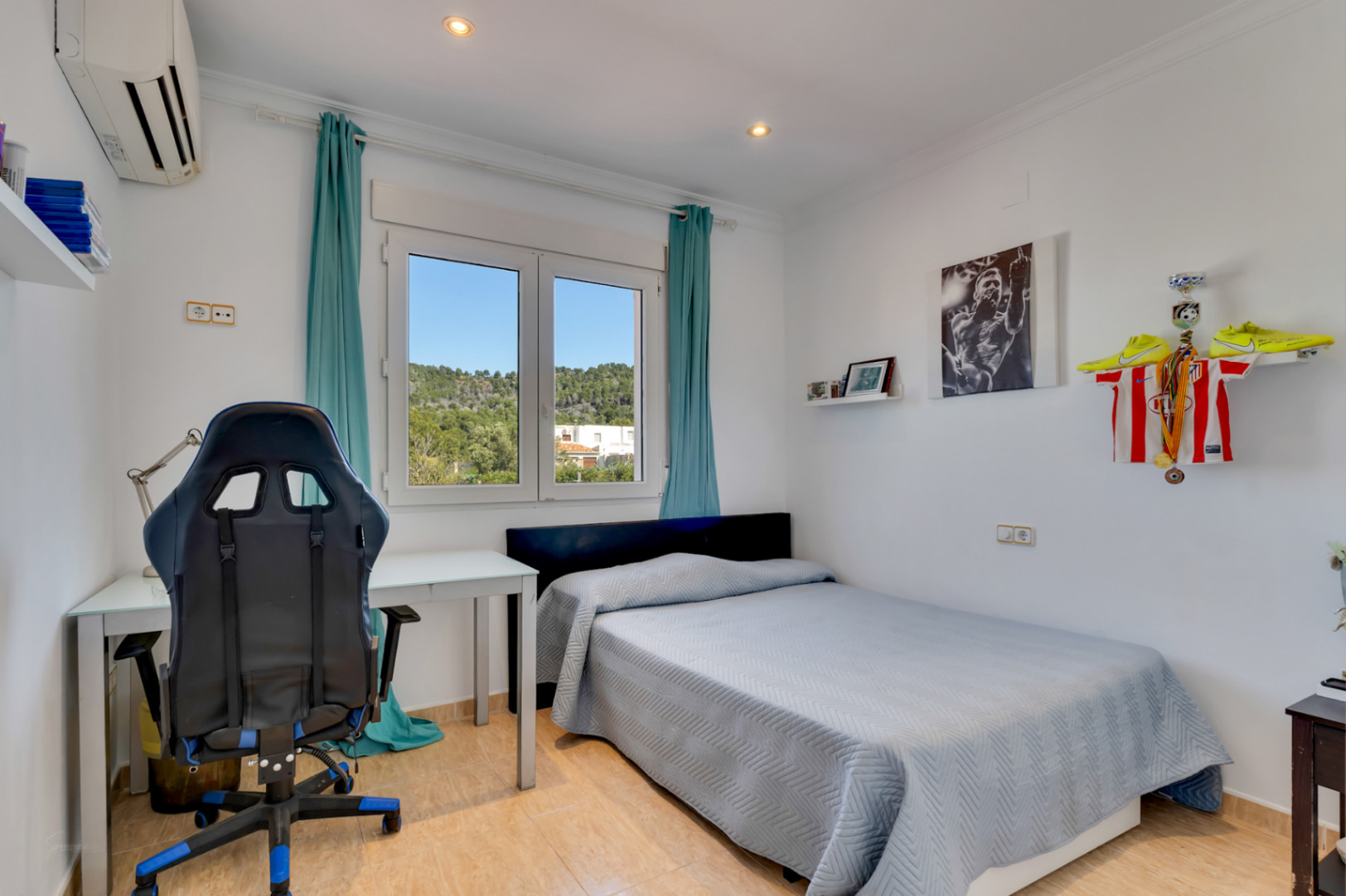 Chambre lumineuse avec coin bureau, climatisation et fenêtre en PVC offrant une vue dégagée sur les collines environnantes et la nature.