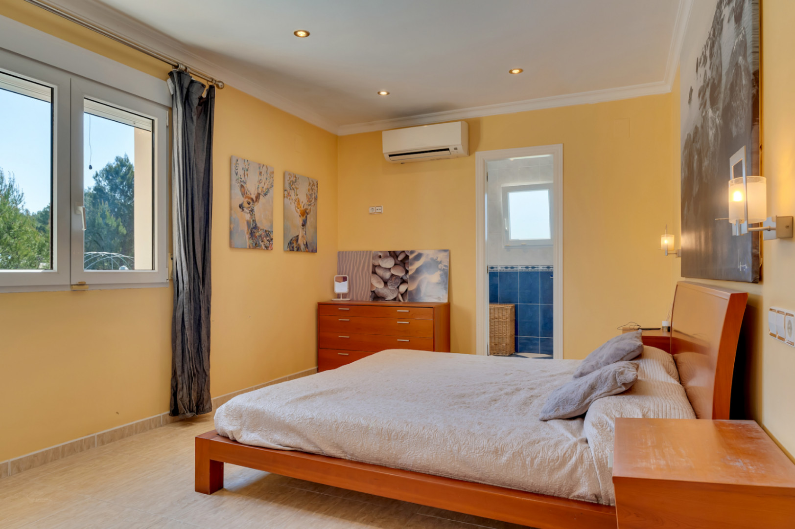 Chambre lumineuse avec salle de bain attenante, climatisation réversible et fenêtre en PVC. Elle dispose de sols en grès, de meubles en bois et de spots encastrés.