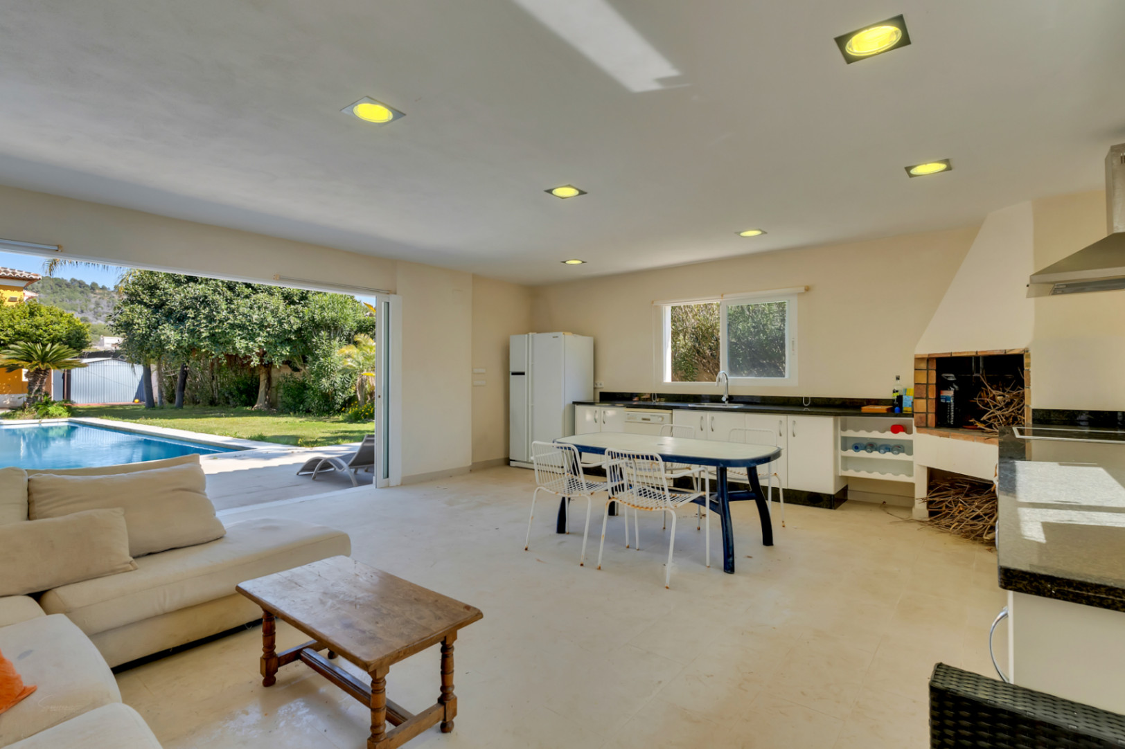 Cuisine d'été et salon décloisonné avec barbecue intégré, plan de travail en granit et larges baies vitrées offrant un accès direct à la piscine et au jardin.