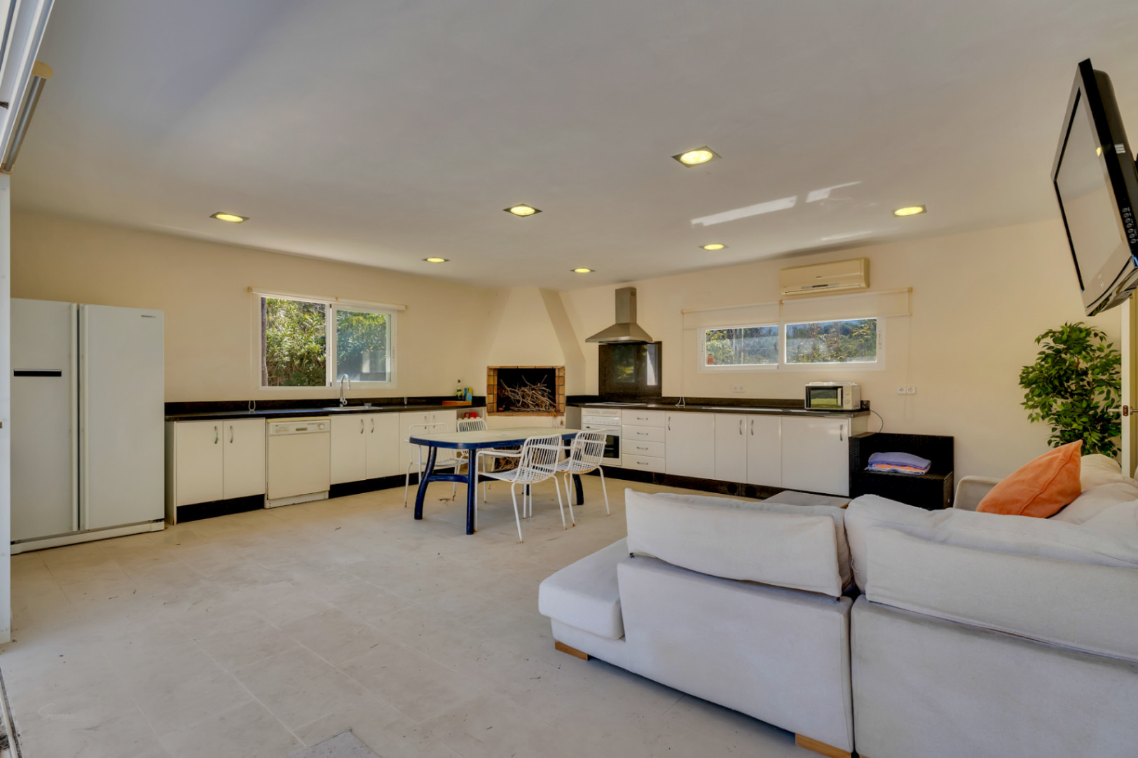 Espace barbecue couvert de 67 m² comprenant une cuisine équipée, une cheminée, un coin repas et un salon climatisé avec carrelage clair.