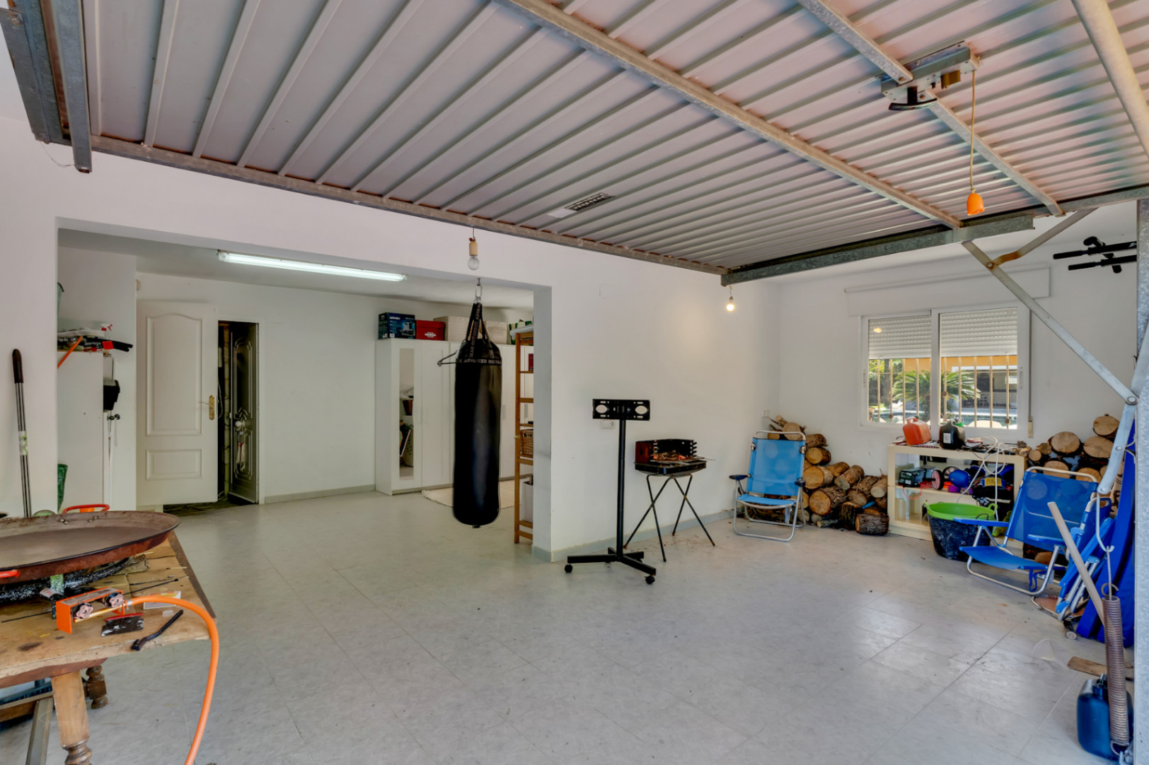 Grand garage avec sol en carrelage et plafond métallique, offrant un espace polyvalent pour le stockage, le sport et un accès direct à la maison.