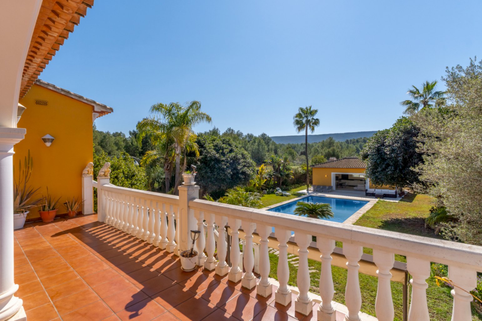 Terrasse à l'étage avec carrelage en terre cuite et balustrade blanche, offrant une vue sur la piscine, le jardin arboré et les paysages naturels environnants.
