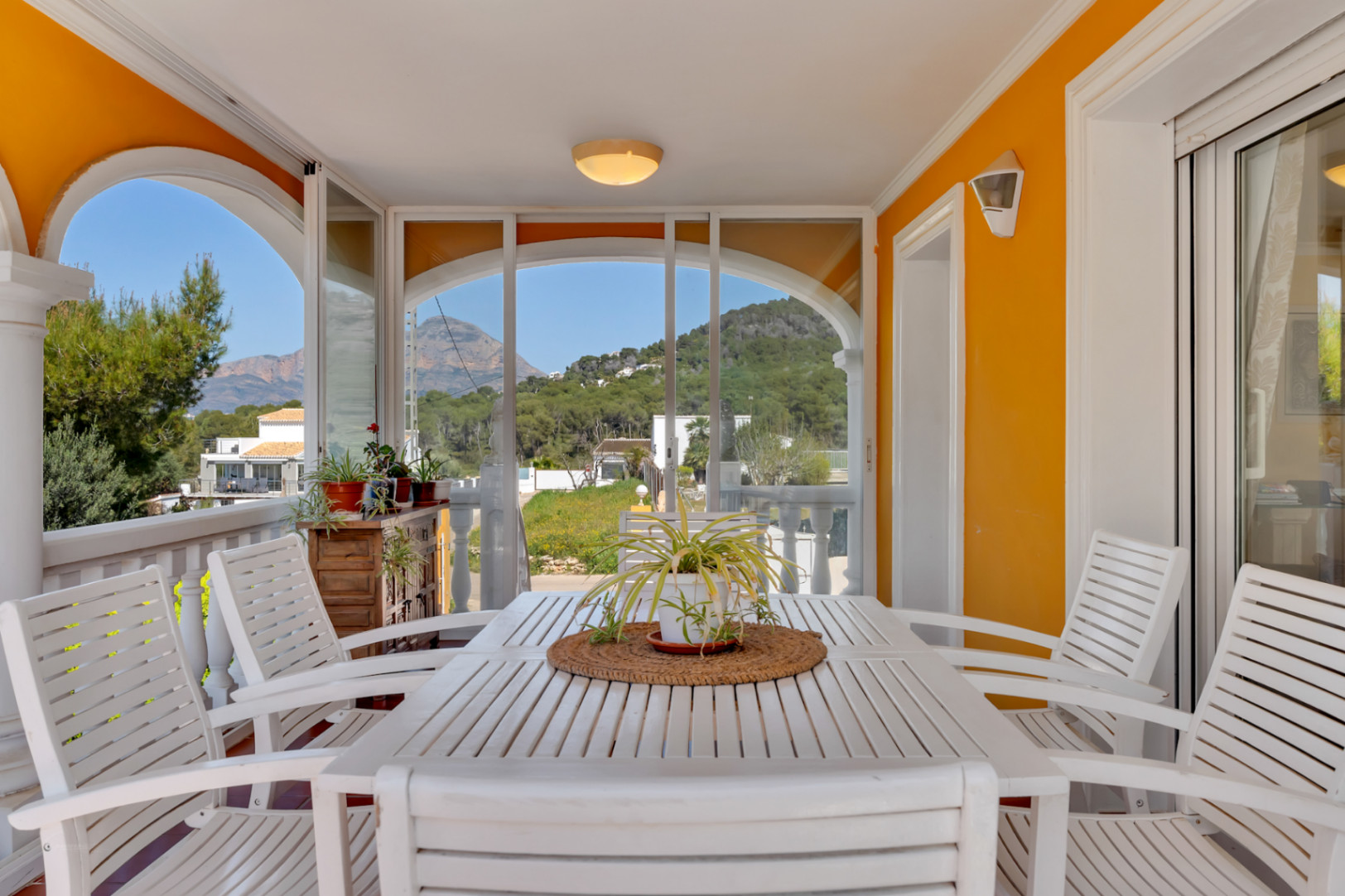 Terrasse couverte avec rideaux de verre, ensemble de salle à manger en bois blanc et vues dégagées sur les montagnes environnantes.