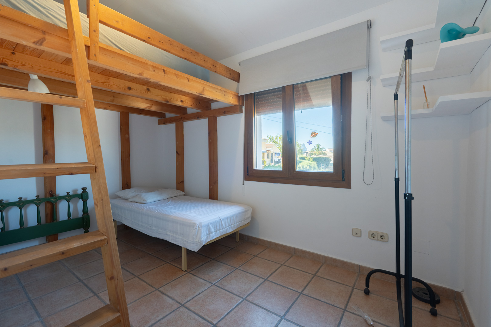 Chambre avec structure de lits superposés en bois massif, sol en grès rustique et fenêtre à cadre en bois offrant une lumière naturelle.