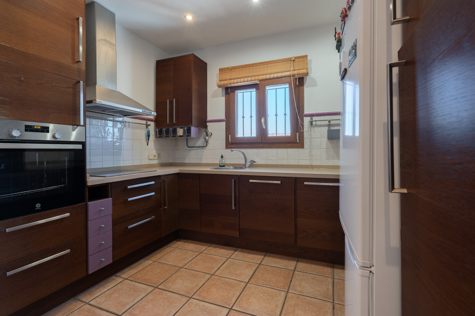 Cuisine fonctionnelle avec placards en bois foncé, four encastré Balay et sol en grès. Équipée d'une hotte en inox et d'une fenêtre avec cadre en bois.