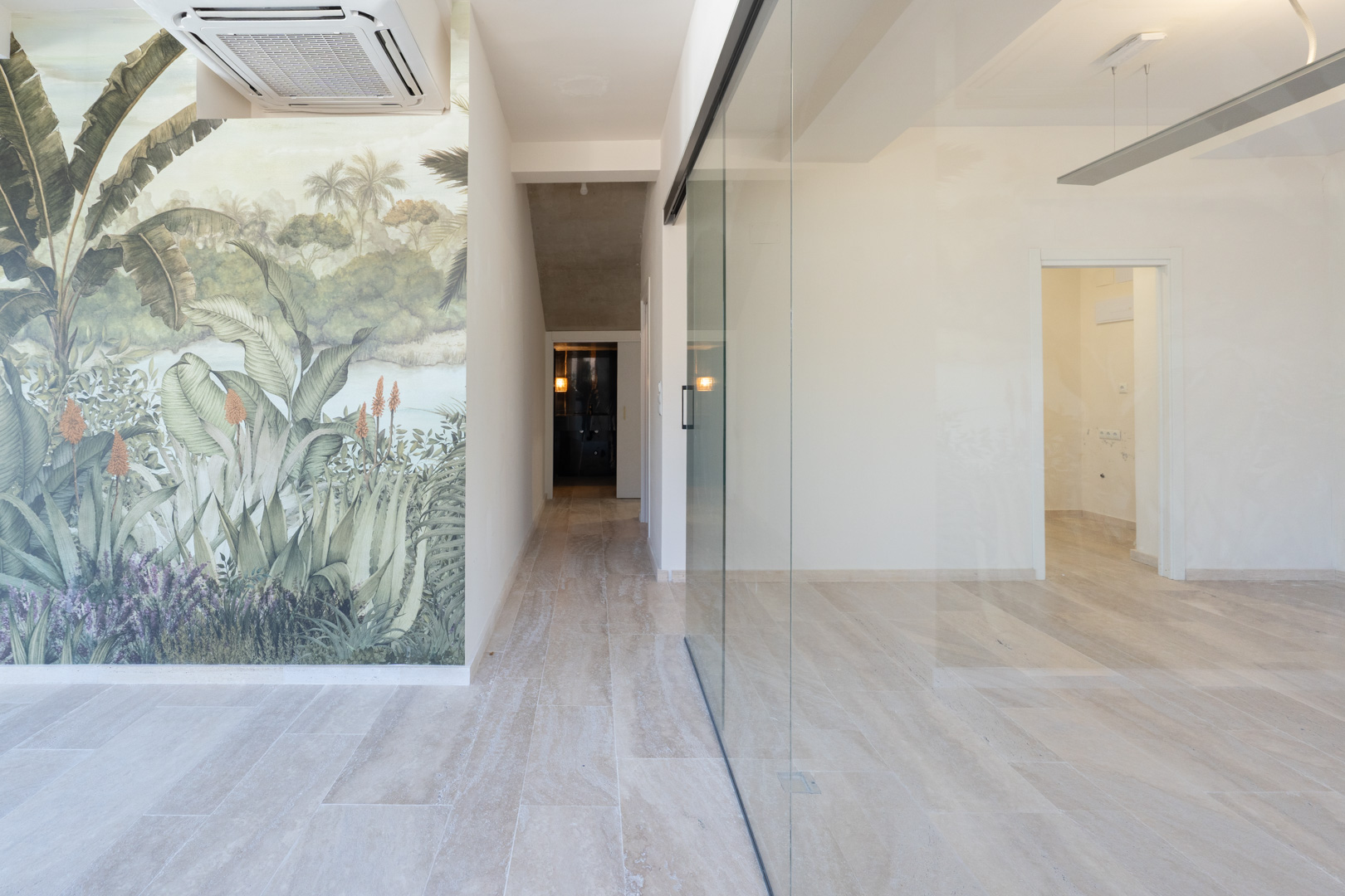 Espace commercial lumineux avec sol en grès, cloison vitrée et mur décoratif à motif tropical. Équipé d'une unité de climatisation à cassette au plafond.