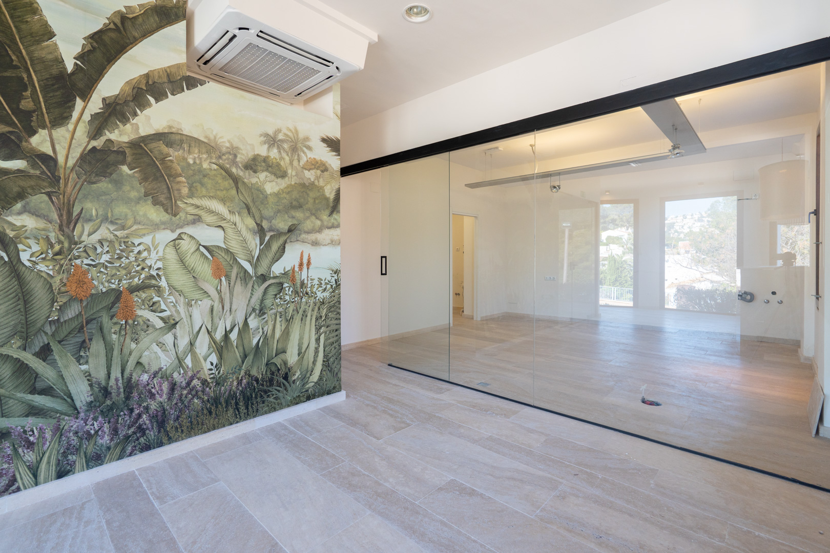 Espace commercial lumineux avec sol en grès, fresque murale tropicale et une grande paroi vitrée coulissante avec encadrement noir pour une division élégante.