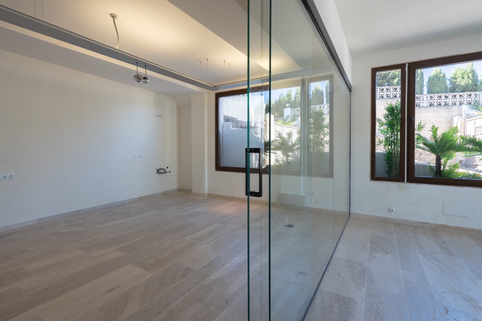 Espace commercial lumineux avec sol en pierre naturelle et une grande paroi vitrée fixe, offrant une vue dégagée sur les extérieurs végétalisés.