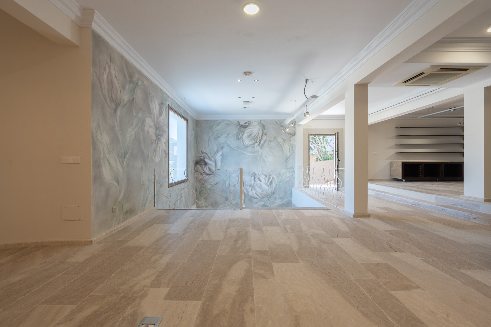 Espace commercial ouvert avec sol en pierre naturelle, murs ornés de fresques florales et garde-corps en fer forgé blanc bordant l'escalier.