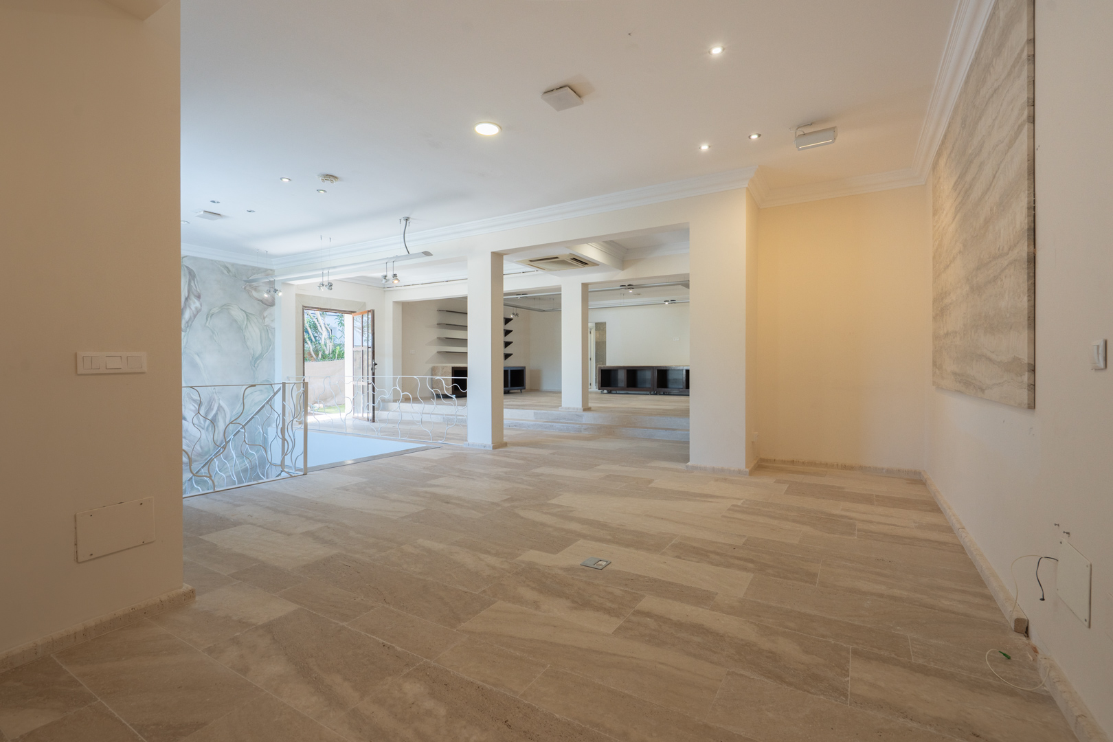 Espace de réception spacieux avec sol en pierre naturelle, éclairage encastré et un escalier avec rampe décorative reliant les niveaux commerciaux.