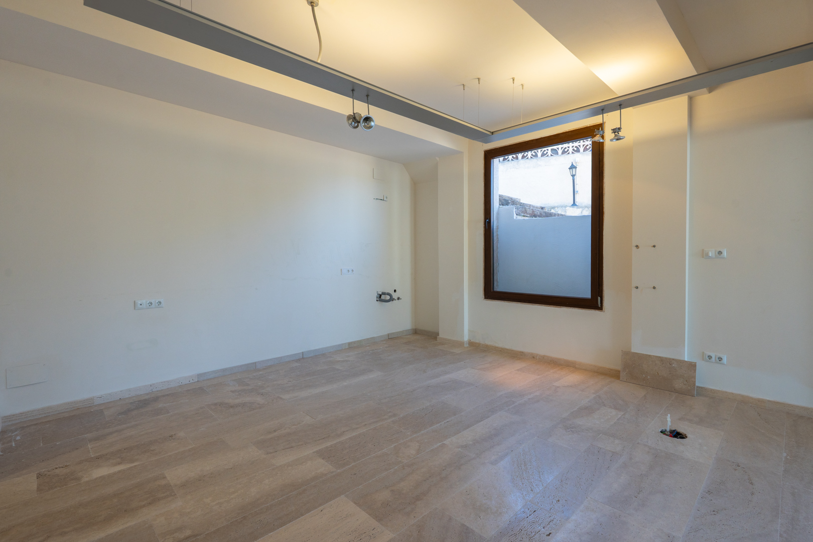 Espace ouvert avec sol en pierre naturelle, système d'éclairage sur rails et raccordements techniques, idéal pour un usage commercial ou de bureau.