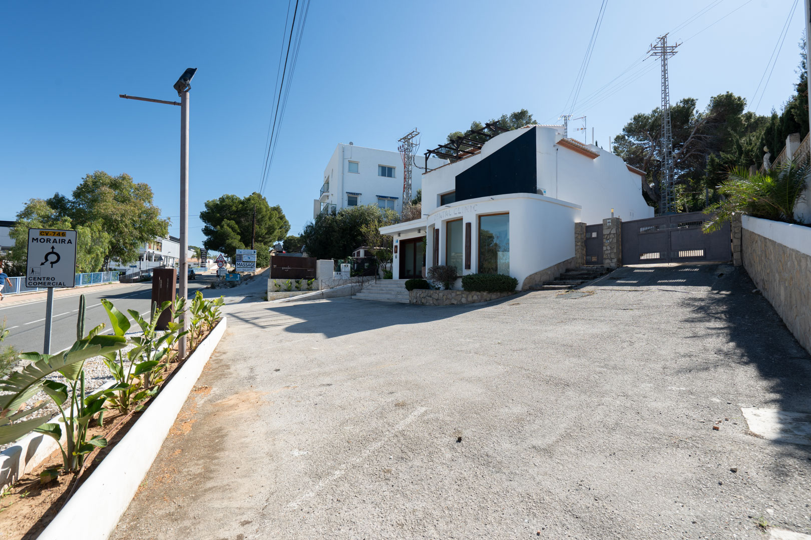 Façade extérieure moderne avec de grandes baies vitrées, un vaste parking privé et un accès direct depuis la route principale Moraira-Calpe.
