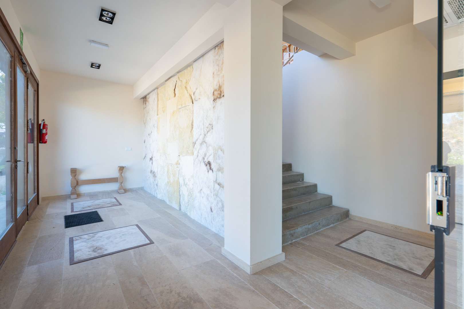 Hall d'entrée avec mur d'accent en pierre naturelle, sol en carrelage avec inserts en marbre et escalier menant aux étages supérieurs.