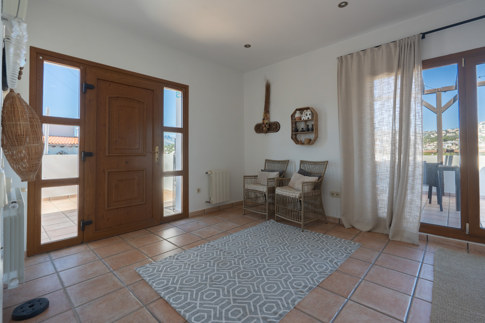 Hall d'entrée lumineux avec carrelage en terre cuite, porte en bois vitrée et accès à une terrasse équipée d'une pergola en bois.