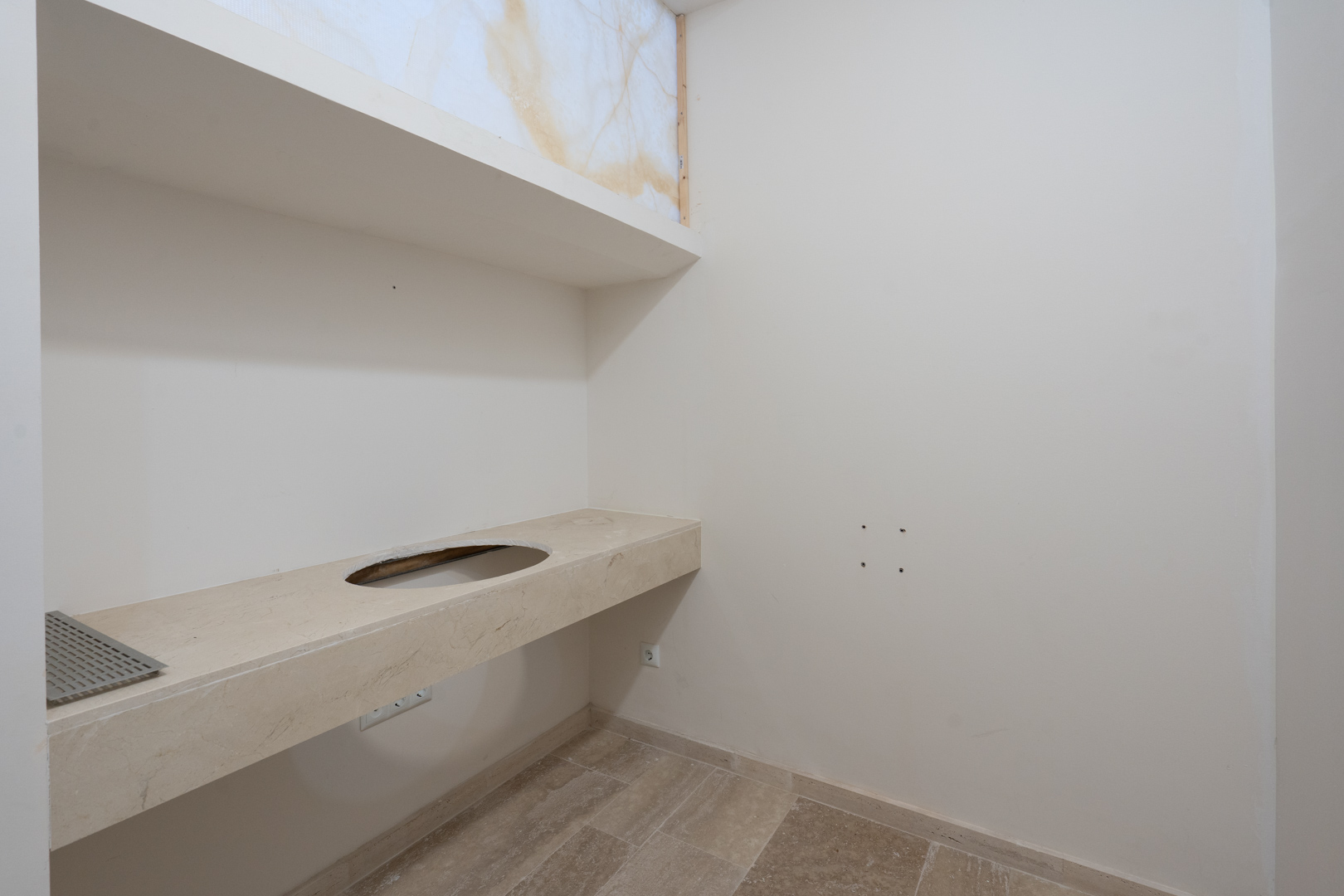 Plan de travail suspendu en pierre naturelle avec découpe pour vasque, surmonté d'une niche murale avec panneau décoratif rétroéclairé et sol en grès.