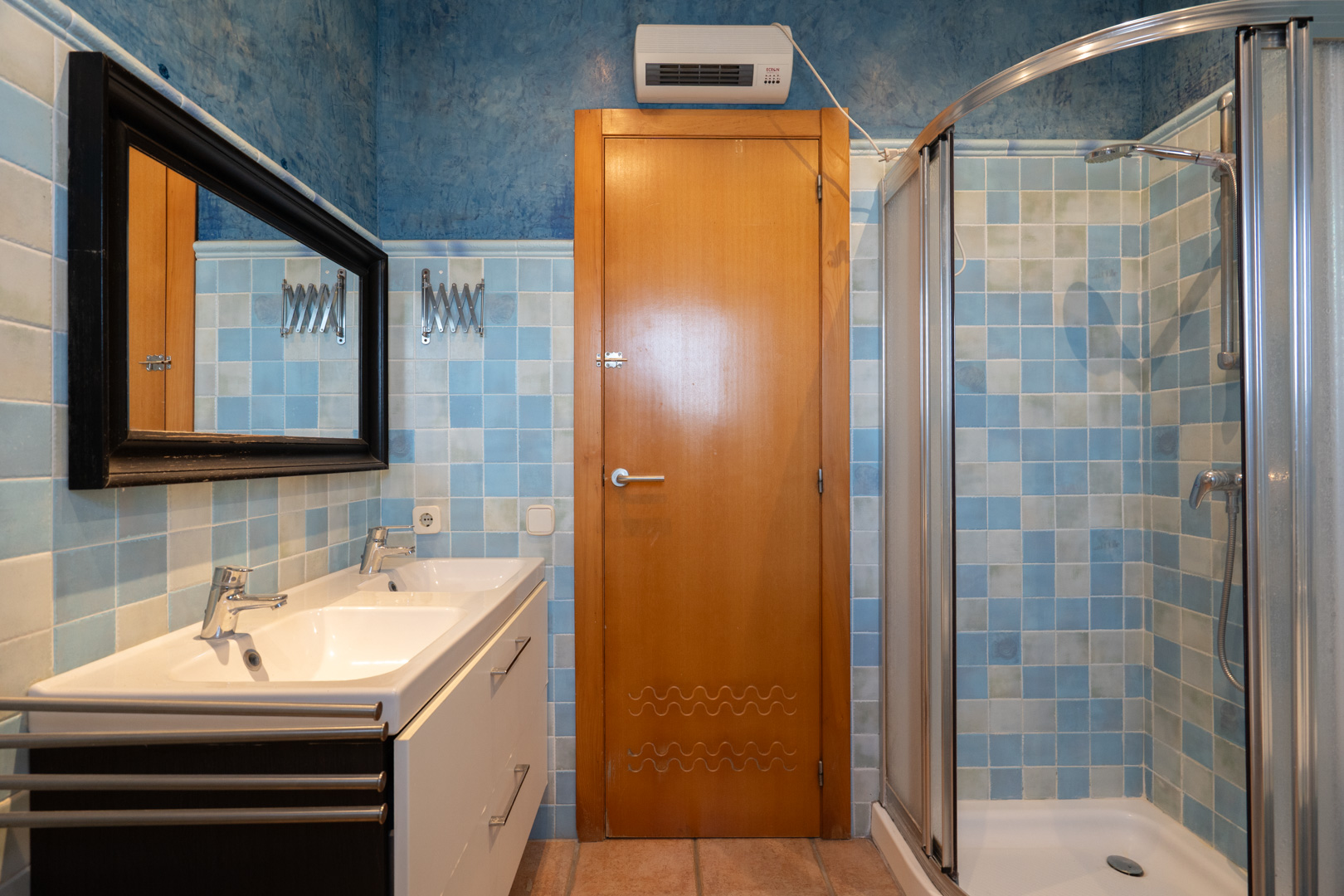Salle de bain avec double vasque, douche d'angle à paroi incurvée et murs carrelés dans des nuances de bleu et blanc.