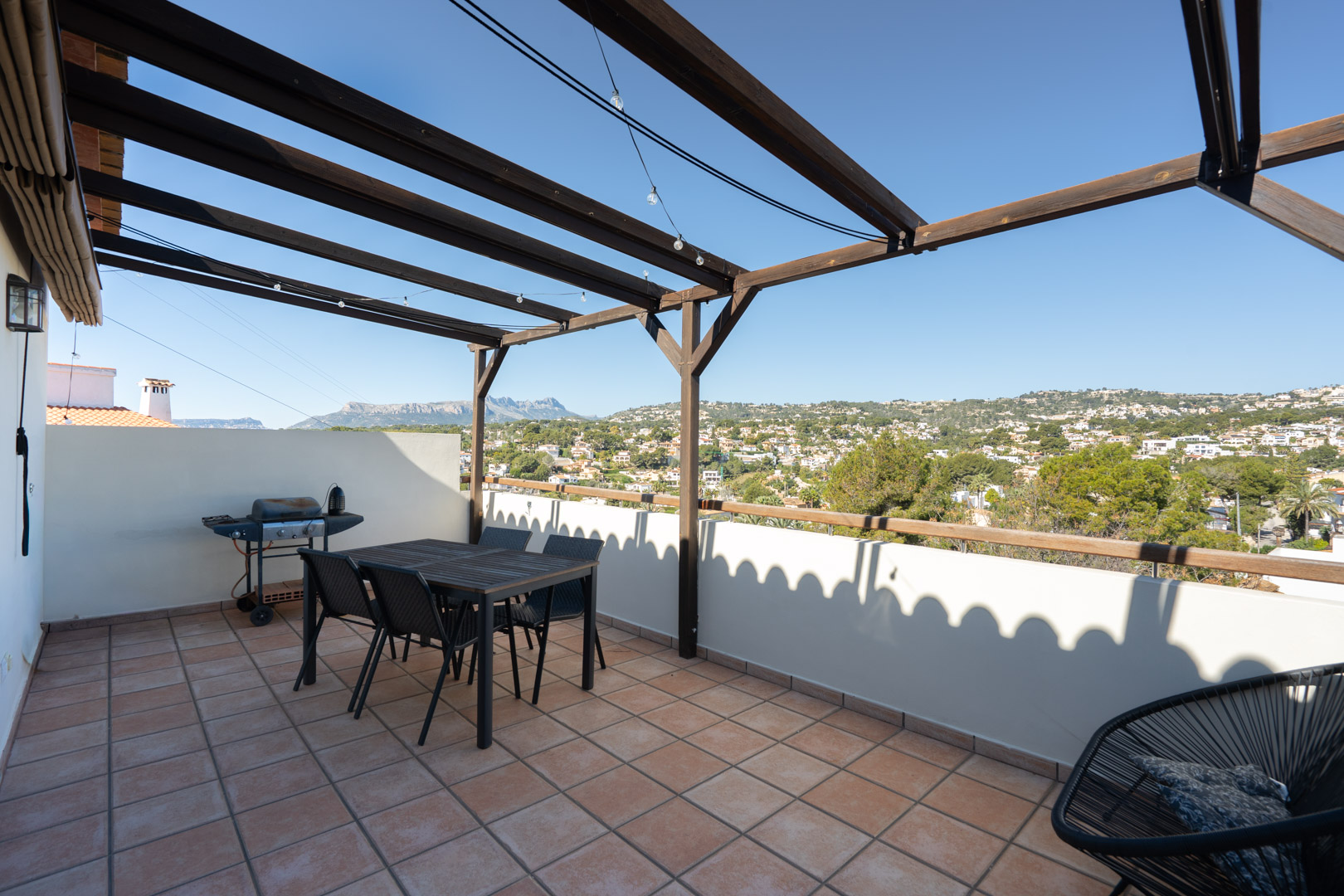 Terrasse à l'étage avec sol en carrelage, pergola en bois et espace repas. Elle offre une vue panoramique sur la Sierra de Bernia et le paysage environnant.
