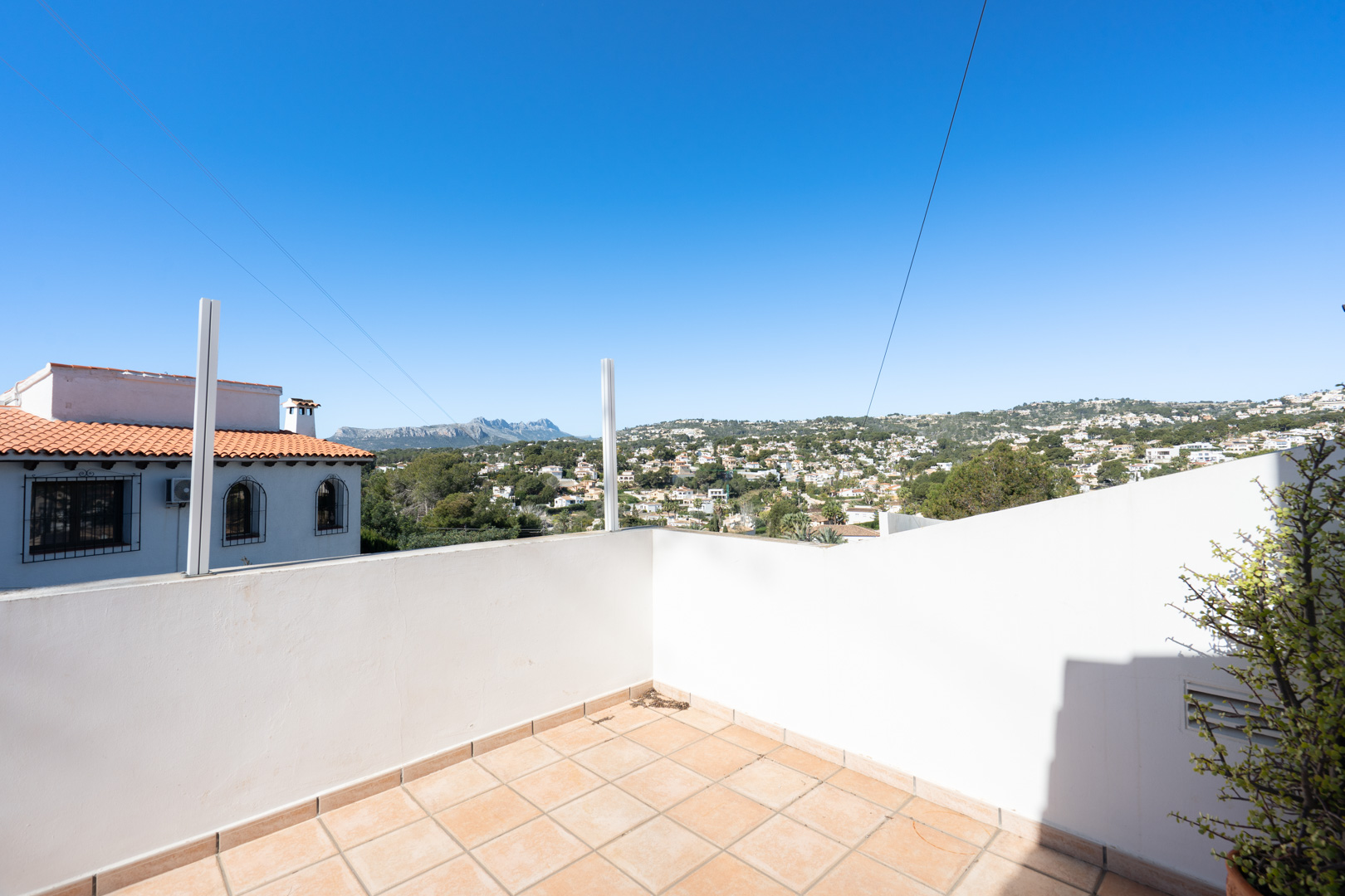 Terrasse extérieure avec revêtement en dalles céramiques et murs blancs, offrant une vue dégagée sur la Sierra de Bernia et le paysage résidentiel environnant.