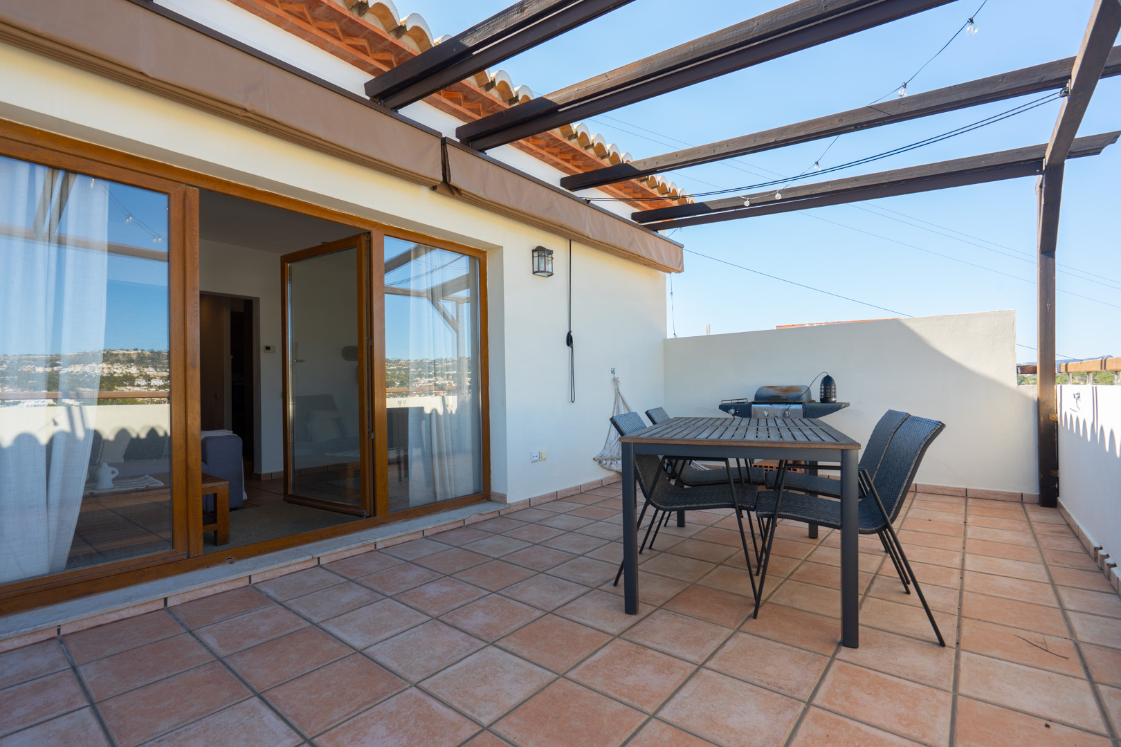 Terrasse supérieure avec carrelage en terre cuite, pergola en bois et espace repas extérieur. De larges baies vitrées assurent la transition vers l'intérieur.