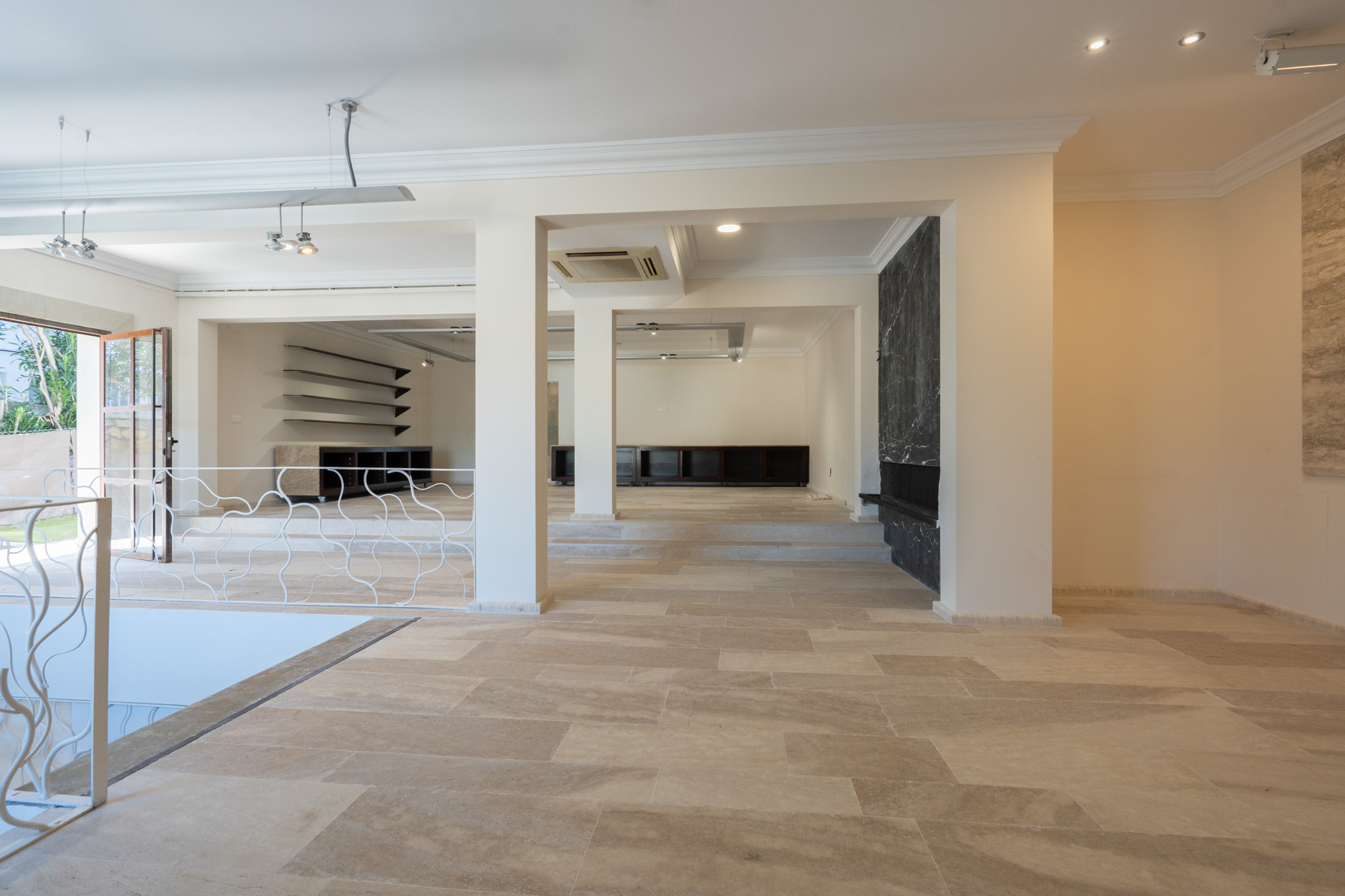 Vaste espace ouvert avec sol en pierre naturelle, niveaux décalés et mur d'accent en marbre noir. Comprend un éclairage encastré et une rampe en fer forgé.