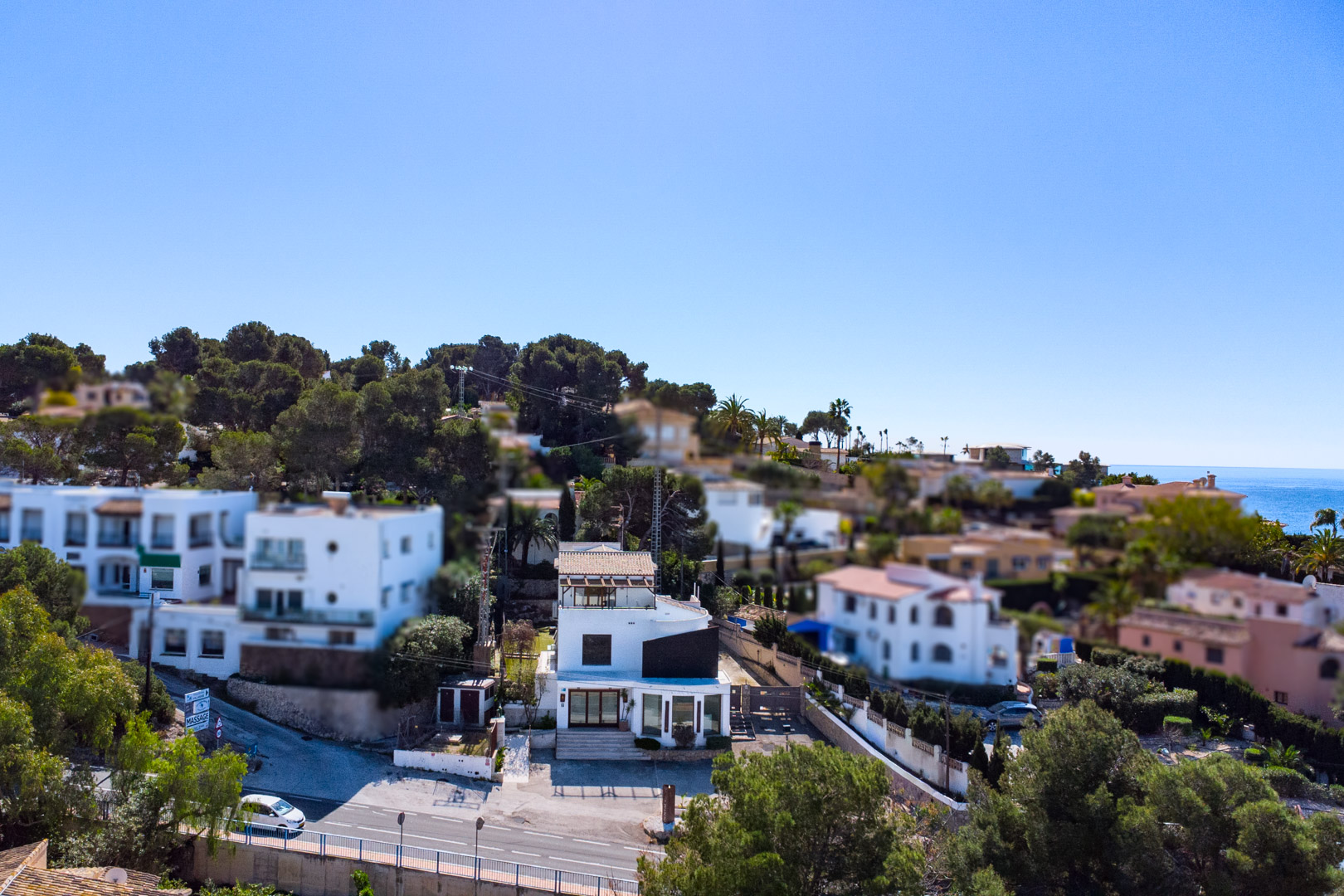 Vue aérienne de la propriété sur la route Moraira-Calpe, avec sa façade blanche, ses vitrines commerciales et un aperçu de la mer Méditerranée.