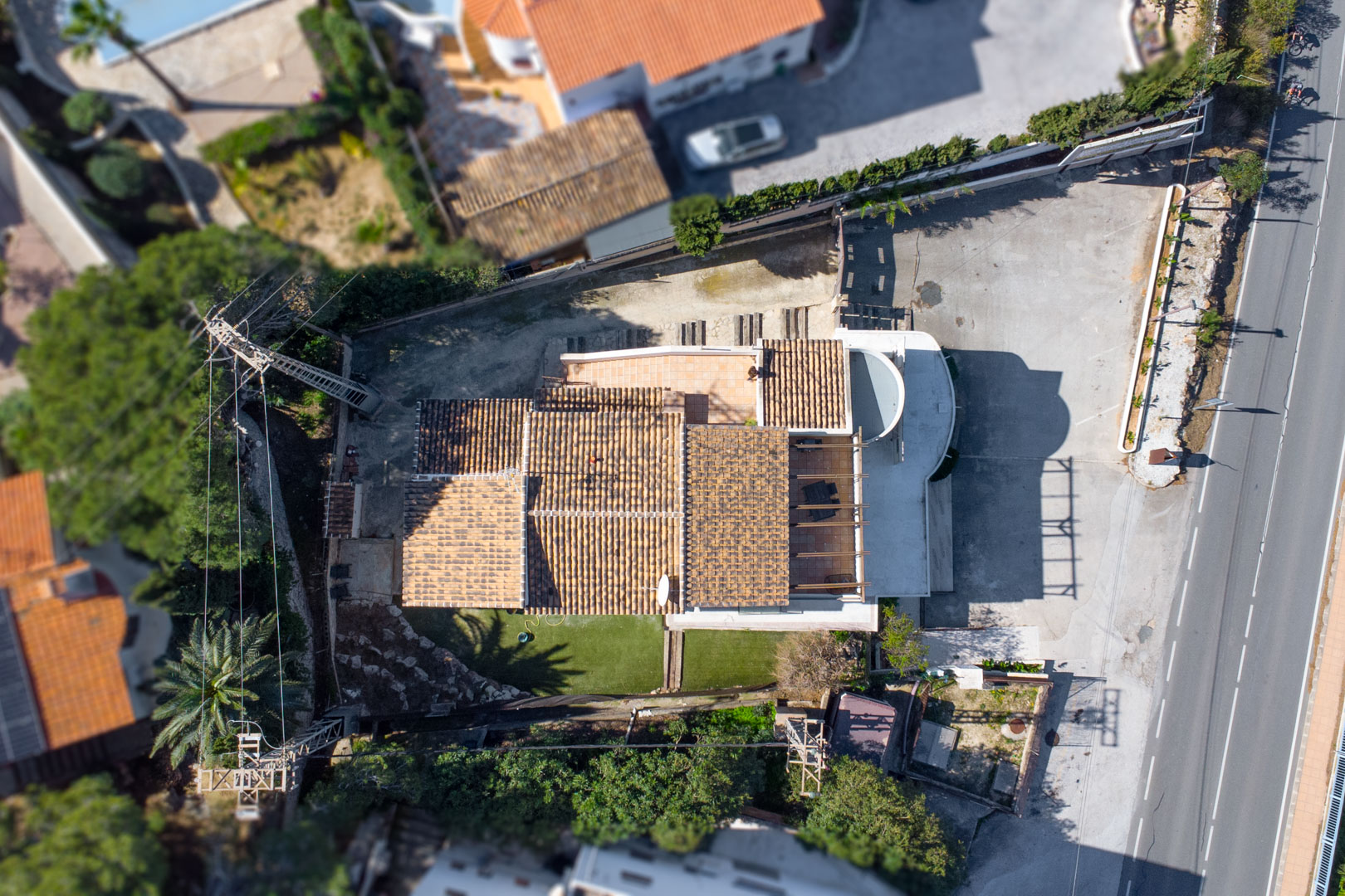Vue aérienne zénithale illustrant la disposition du bâtiment, ses toits en tuiles, les terrasses et le vaste parking privé situé en bordure de l'axe principal.