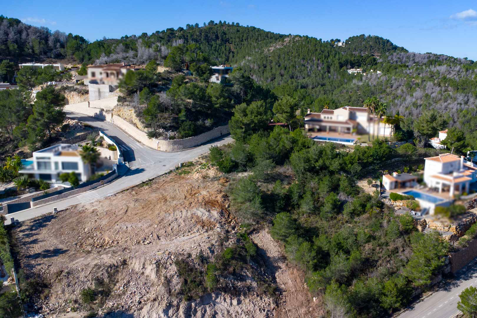 Vue aérienne du terrain surélevé entouré de forêts de pins, montrant le site de construction préparé et les villas voisines avec piscines privées.