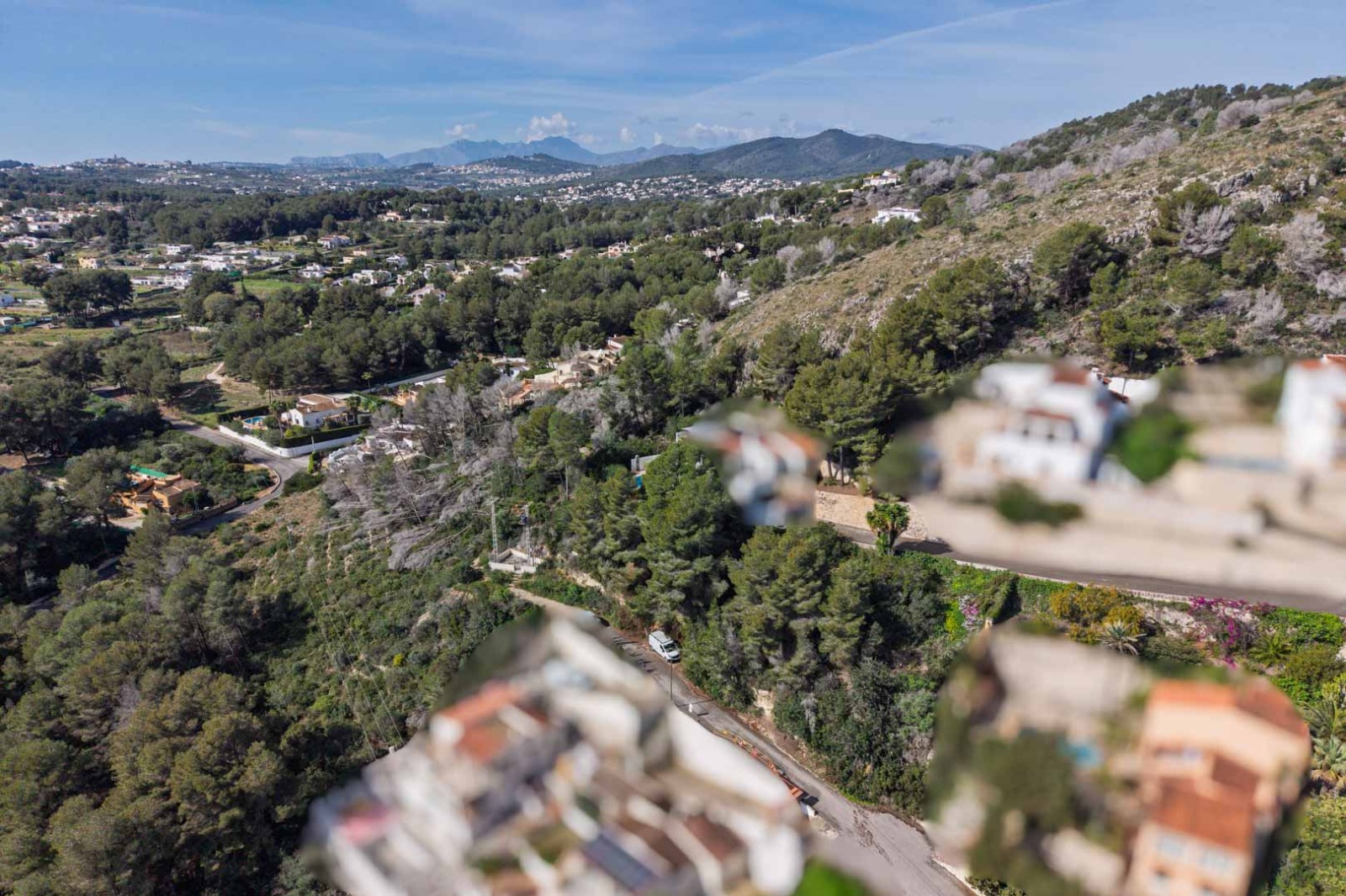 Vue aérienne de l'urbanisation Sol de Este, mettant en valeur la forêt de pins dense, les collines environnantes et les montagnes au loin sous un ciel dégagé.
