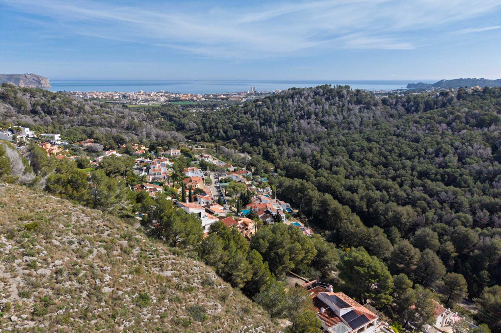 Vue aérienne panoramique illustrant la topographie élevée surplombant des collines boisées, avec une vue dégagée sur la mer Méditerranée et le littoral de Jávea.
