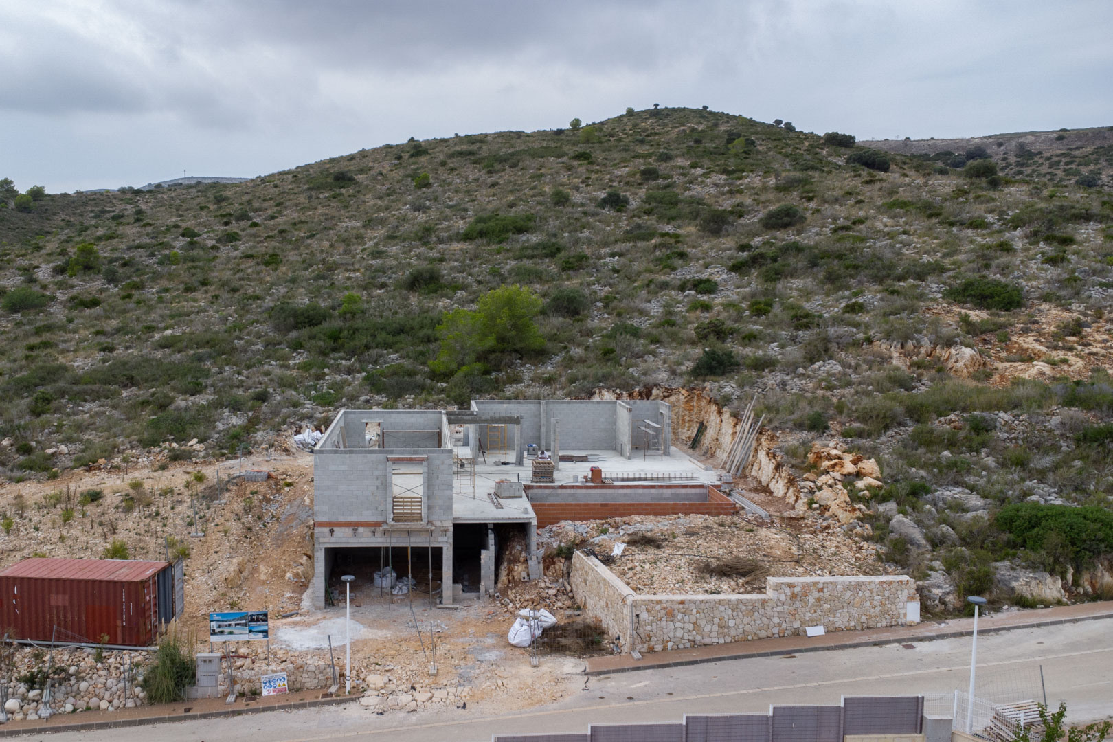 Phase de construction d'une villa à Pedreguer, montrant les structures en blocs de béton, un mur d'enceinte en pierre naturelle et l'implantation en colline.