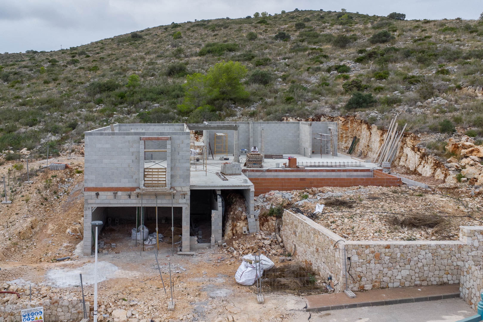 Phase de gros œuvre d'une villa moderne à Pedreguer, illustrant la structure en béton, les murs en pierre naturelle et l'intégration au terrain.