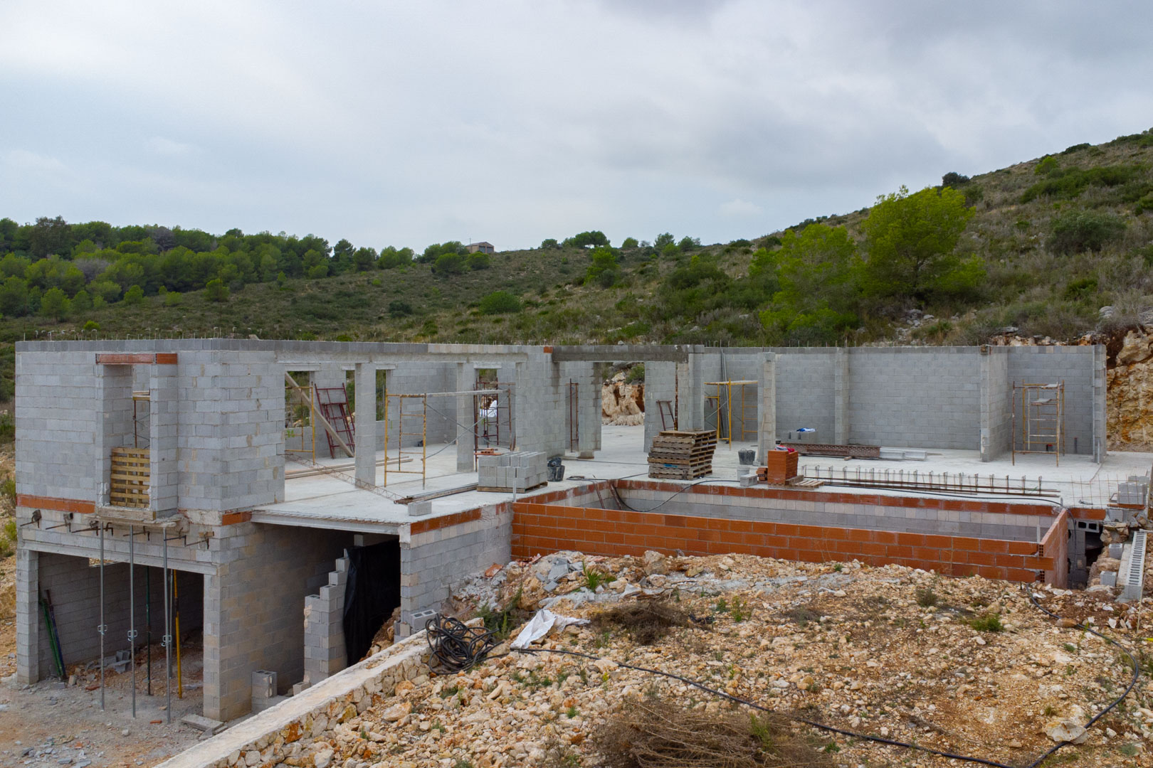 Villa moderne en cours de construction à Pedreguer, avec murs en parpaings, structure de piscine et emplacement surélevé à flanc de colline.