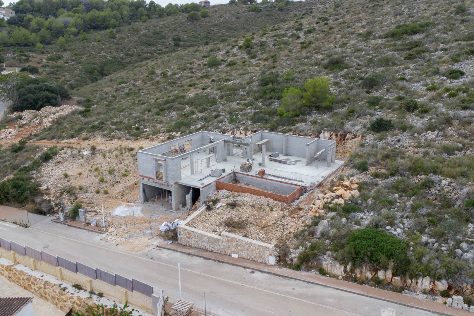 Vue aérienne de l'avancement des travaux de la villa à Pedreguer, montrant la structure en parpaings et les fondations intégrées à la colline naturelle.
