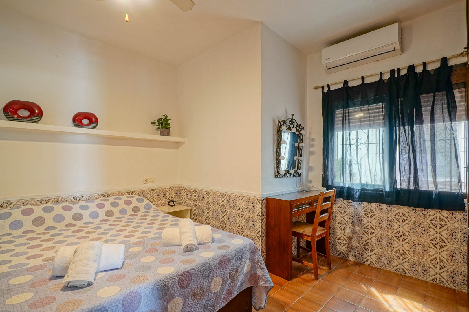 Chambre avec soubassement en faïence décorative, bureau en bois et miroir éclairé. Équipée de la climatisation et d'un sol en grès rustique.