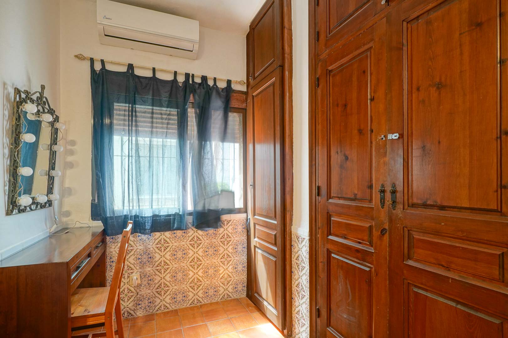 Coin coiffeuse avec bureau en bois et miroir éclairé, jouxtant de grands placards intégrés en bois sombre et un soubassement en carreaux de faïence traditionnels.