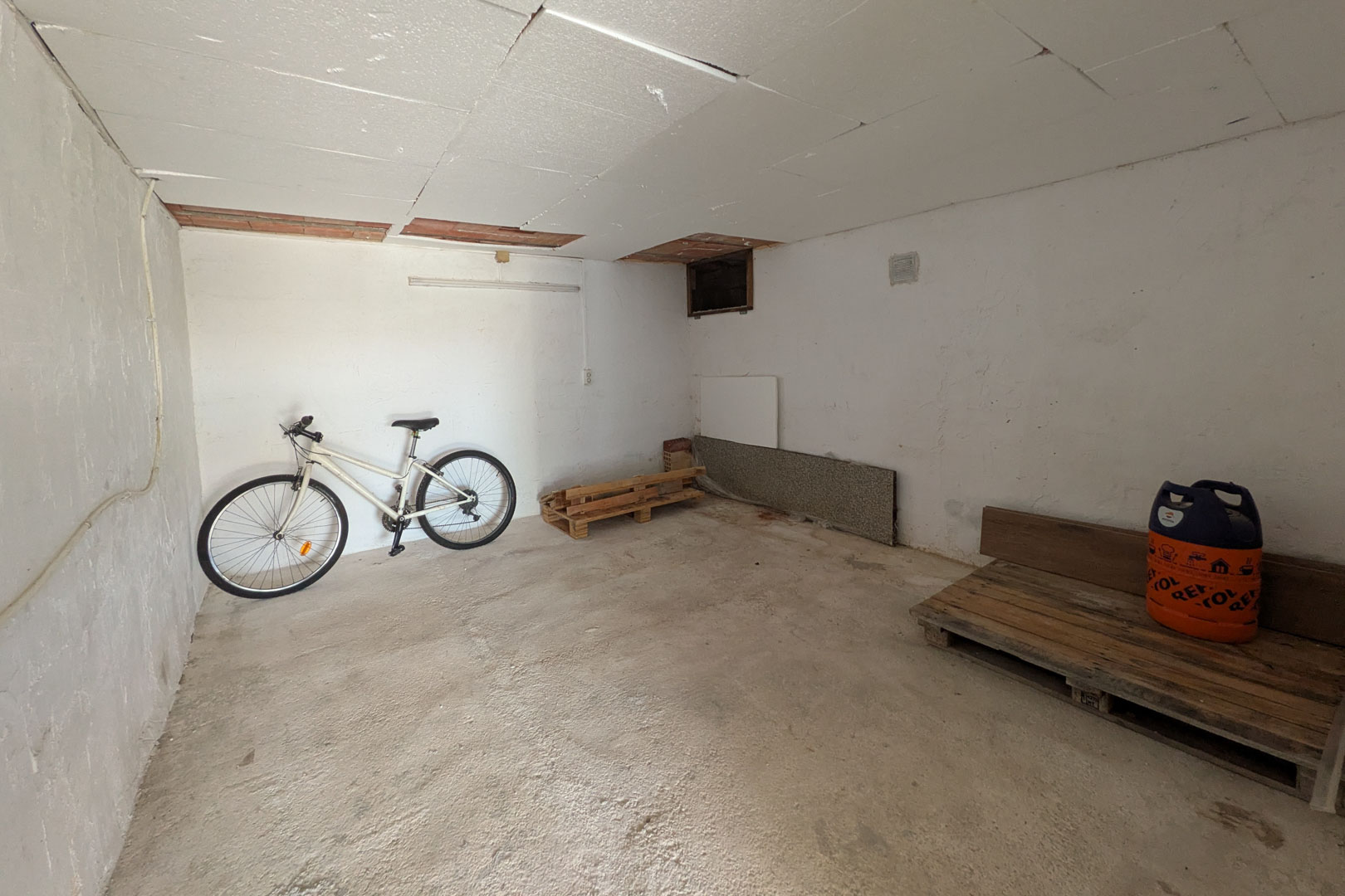 Débarras indépendant avec plafonds à panneaux, sol en ciment et espace polyvalent pour le stockage de vélos ou de matériel.