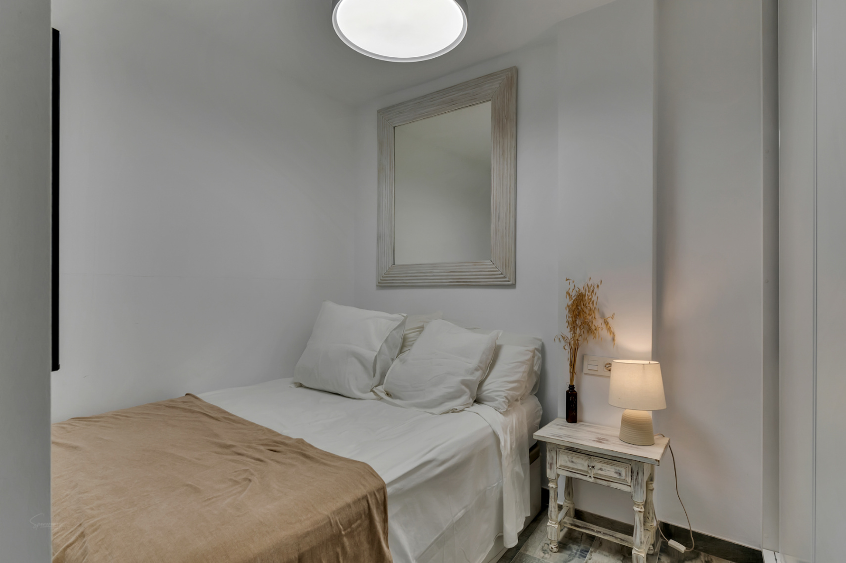 Chambre lumineuse avec miroir décoratif et table de chevet de style vintage.