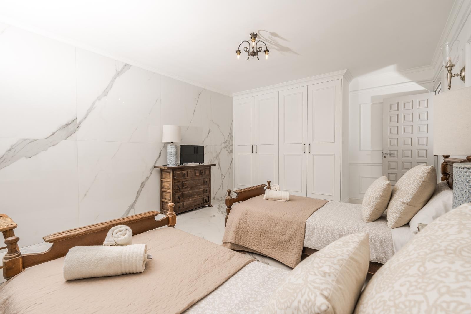 Chambre avec deux lits jumeaux en bois, un mur d'accent en marbre veiné et des placards intégrés blancs. Le mobilier rustique s'harmonise avec les finitions modernes.