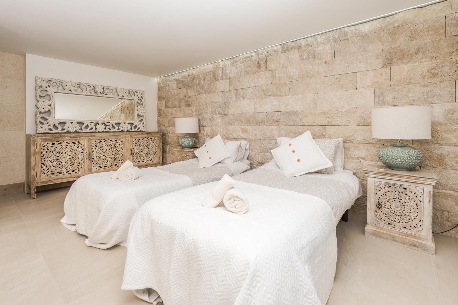 Chambre avec lits jumeaux offrant un mur en pierre naturelle, du mobilier en bois sculpté à la main et un éclairage d'ambiance soigné.