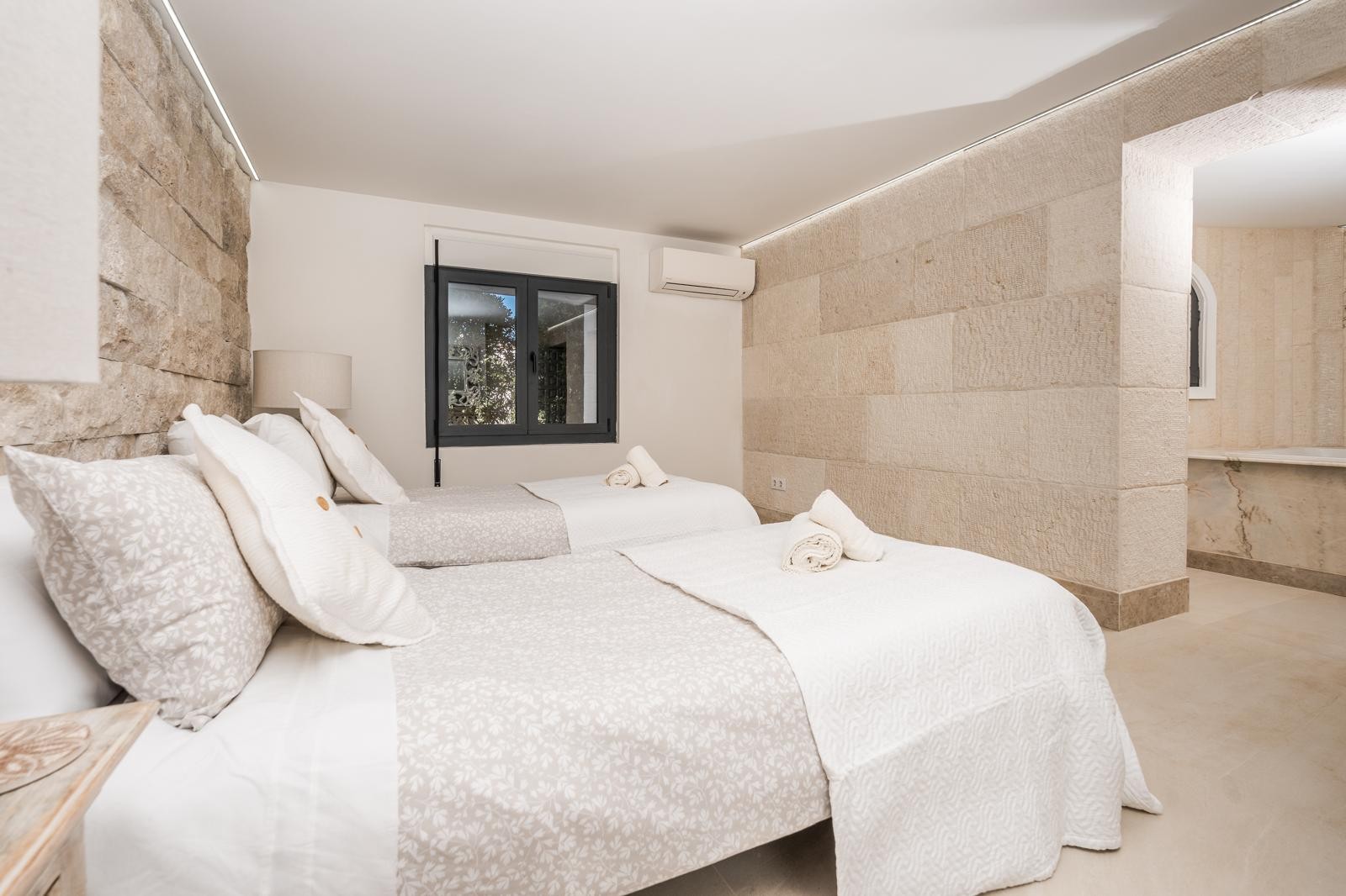 Chambre avec murs en pierre naturelle, deux lits simples, éclairage LED intégré et salle de bain attenante avec finitions en marbre.