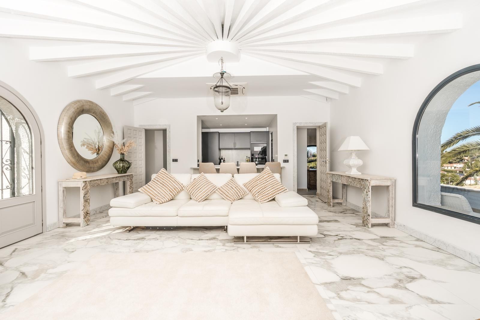 Espace de vie circulaire avec poutres de plafond radiales, sol en marbre et grande fenêtre cintrée. La pièce communique avec la cuisine et bénéficie d'une lumière naturelle optimale.