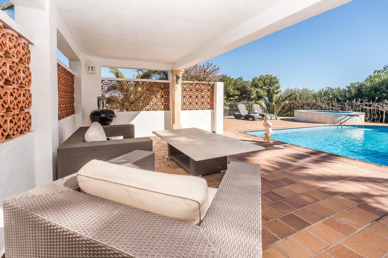 Porche couvert avec salon en rotin et parois en treillis de terre cuite, offrant une vue sur la piscine rénovée et le jacuzzi extérieur.