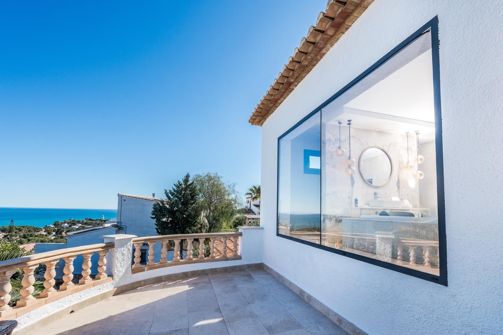 Terrasse supérieure avec balustrade en pierre et vue mer, jouxtant une large baie vitrée dévoilant une salle de bain moderne en marbre et luminaires design.