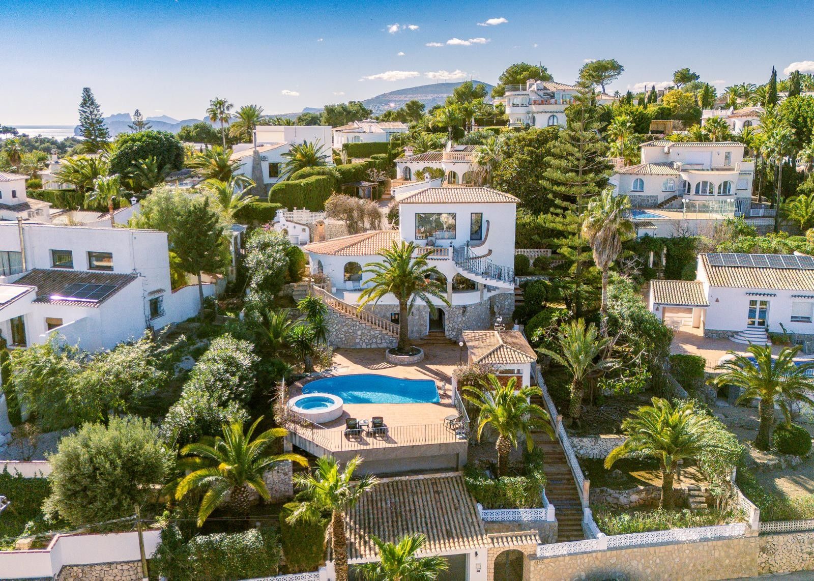 Vue aérienne de la villa dévoilant ses trois niveaux, sa piscine avec jacuzzi, ses terrasses en pierre et son jardin méditerranéen planté de palmiers face au littoral.
