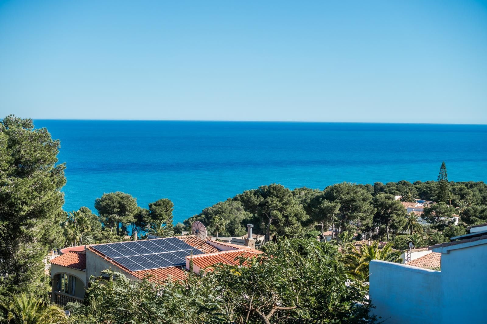 Vue panoramique sur la mer Méditerranée depuis Balcón al Mar, surplombant une pinède dense et des toitures équipées de panneaux photovoltaïques.