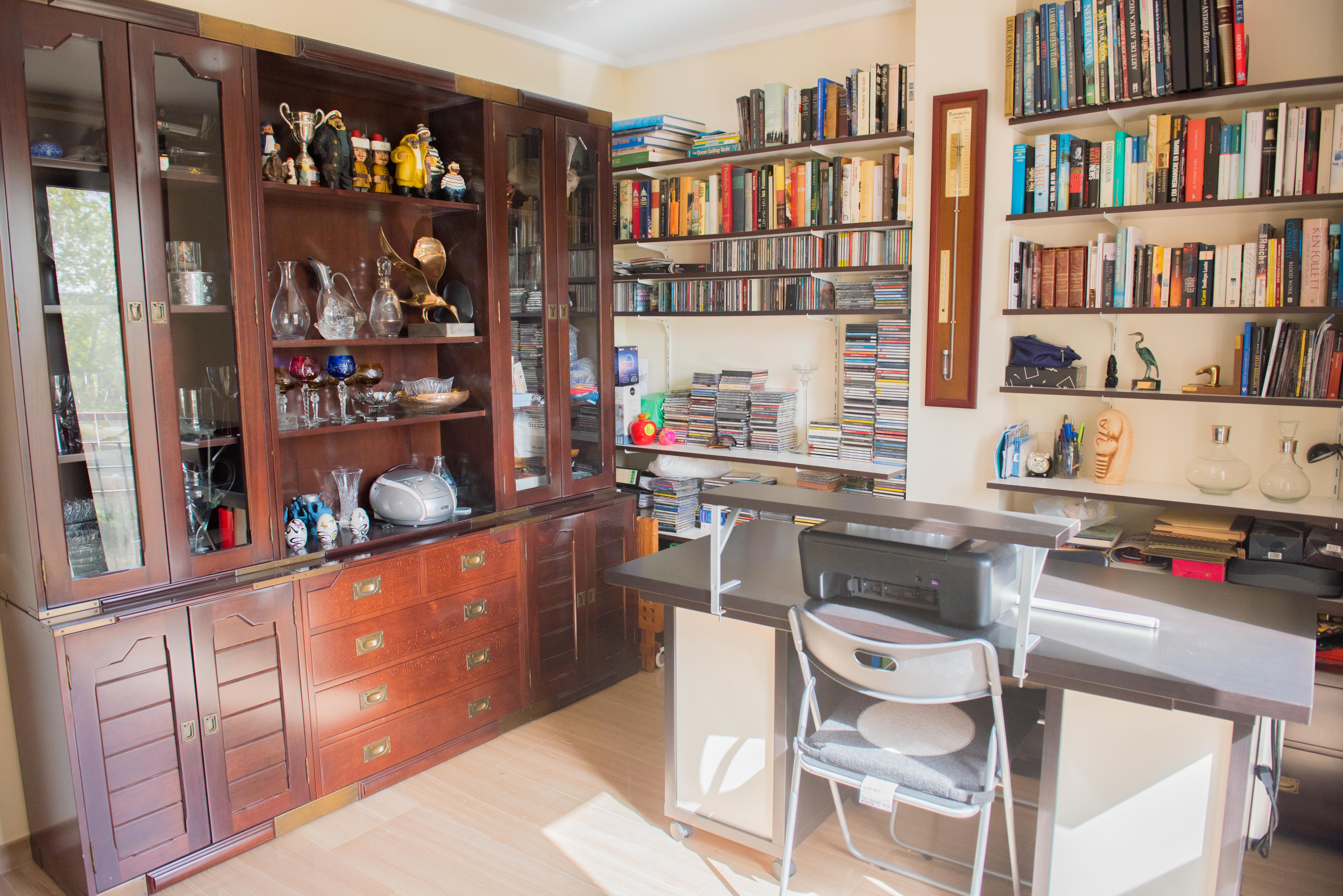 Bureau à domicile comprenant une grande vitrine en bois sombre, des étagères murales chargées de livres et un espace de travail avec sol en grès clair.