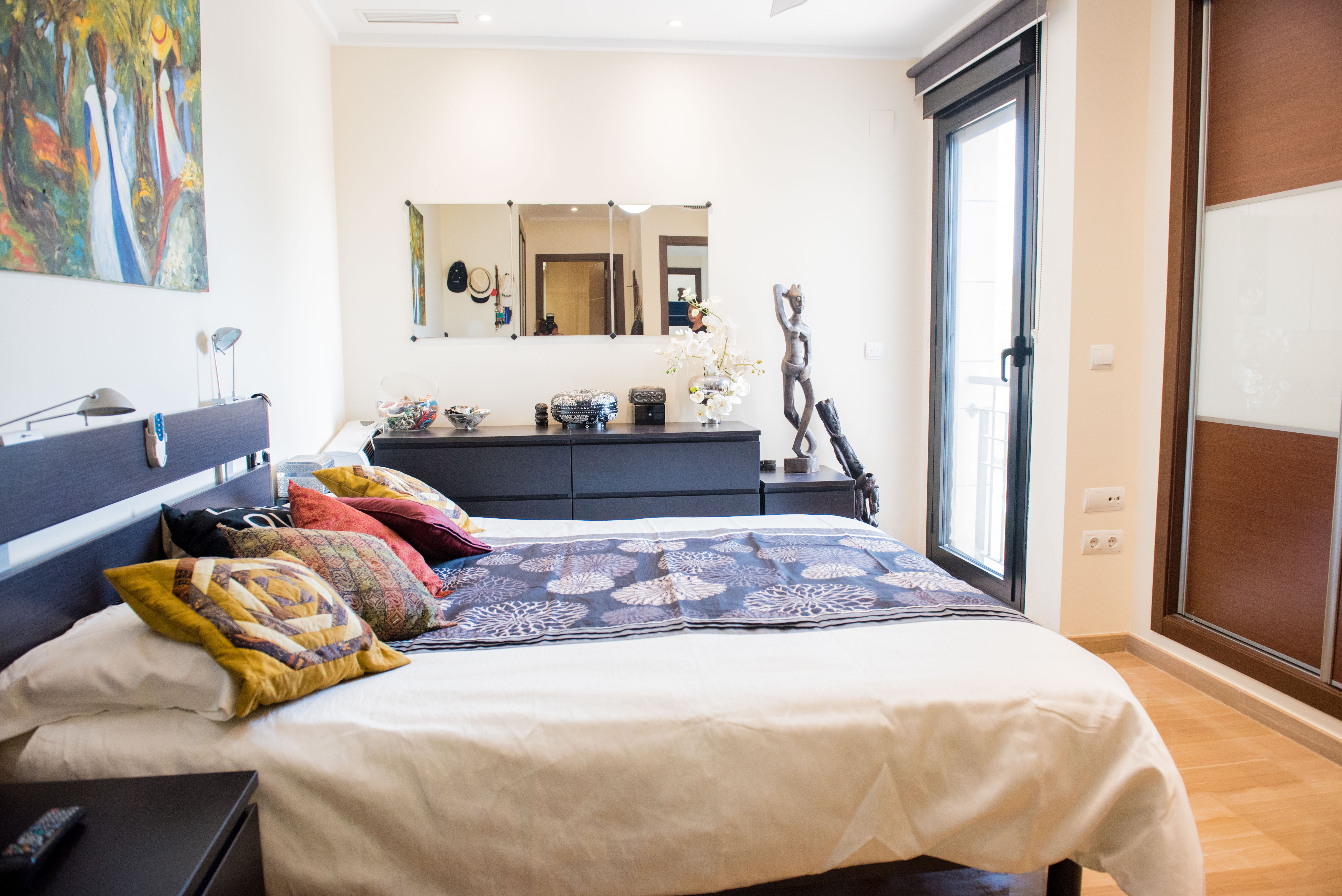 Chambre avec mobilier en bois sombre, placards intégrés et porte vitrée. L'espace comprend une commode avec miroir et un sol en bois clair.